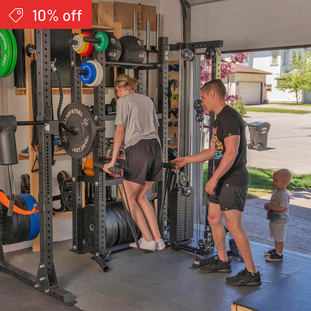 A woman does dips on gym equipment in a home garage where Bells of Steel’s Hydra Storage Builder shelves are visible. A man spots her, a child stands nearby, and a "10% off" discount banner appears in the top left corner.