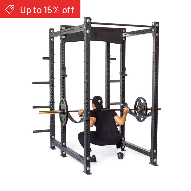 A person in black workout clothes squats with a barbell inside the Bells of Steel Hydra Six Post Power Rack Builder (3" x 3", ⅝" Holes) with weight plate storage. A red banner says "Up to 15% off." Perfect for any home gym.