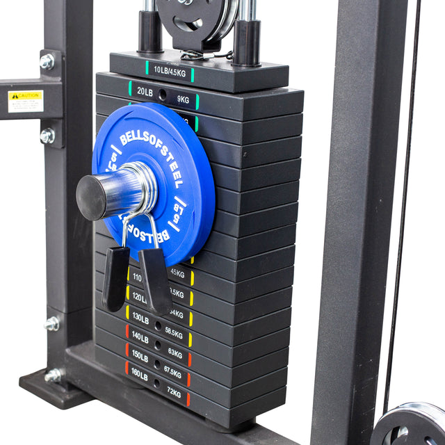 A stack of black weight plates on a gym machine is labeled in pounds and kilograms. A blue 15 lb Bells of Steel plate is micro loading the stack, secured with a Bells of Steel Weight Stack Pin and a silver collar.