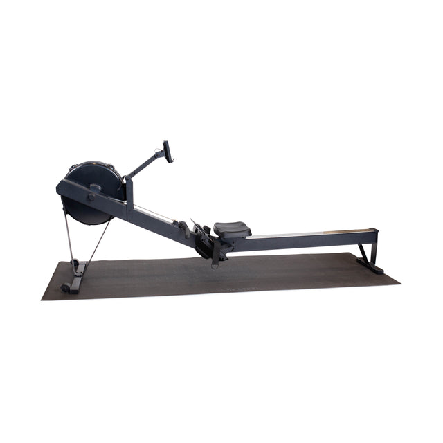A black indoor rowing machine is displayed on a Bells of Steel Cardio Machine Floor Mat, isolated on a white background. The rower features a flywheel, handle, seat, and long rail for smooth workouts.