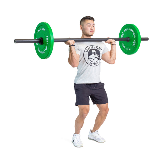 A person in a gray T-shirt and black shorts lifts Bells of Steel Axle Bars with green weights at shoulder height on a white background, showcasing strongman training and impressive grip strength.
