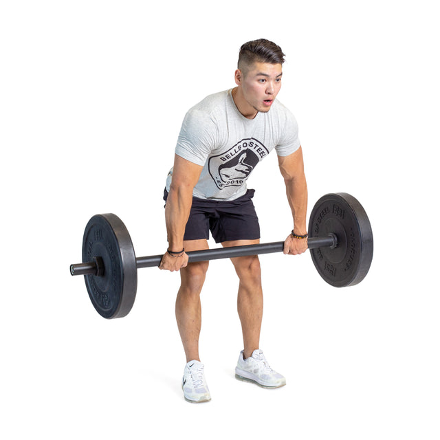 A man wearing a gray T-shirt, black shorts, and white sneakers showcases grip strength by lifting Bells of Steel Axle Bars with a weighted barbell, standing with knees slightly bent and arms extended against a white background.