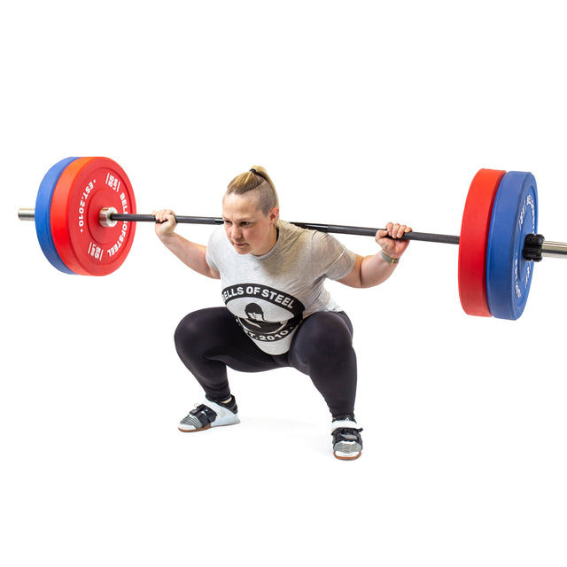 A person in a gray Bells of Steel shirt and black leggings performs a deep barbell squat with Bells of Steel Coloured Bumper Plate Sets, featuring stainless steel inserts, against a white background.