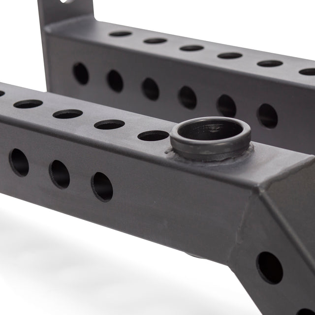 Close-up of Bells of Steel Front Foot Stabilizers: black metal frame with multiple round holes in two parallel bars and a circular holder attached, designed for use with gym power racks for added stability during strength training.