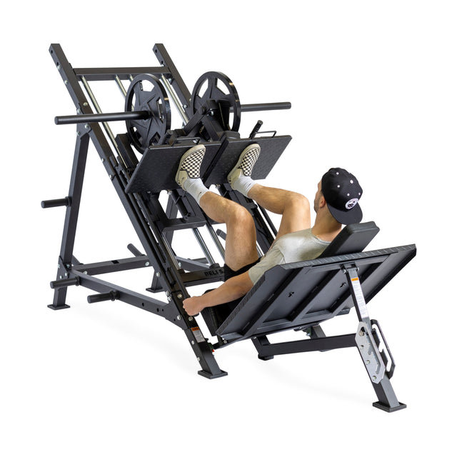 A person in athletic gear uses the Bells of Steel 2-in-1 Iso Leg Press & Hack Squat Machine (The Juggernaut), pressing upward with both feet while seated on a padded bench amid commercial gym equipment.