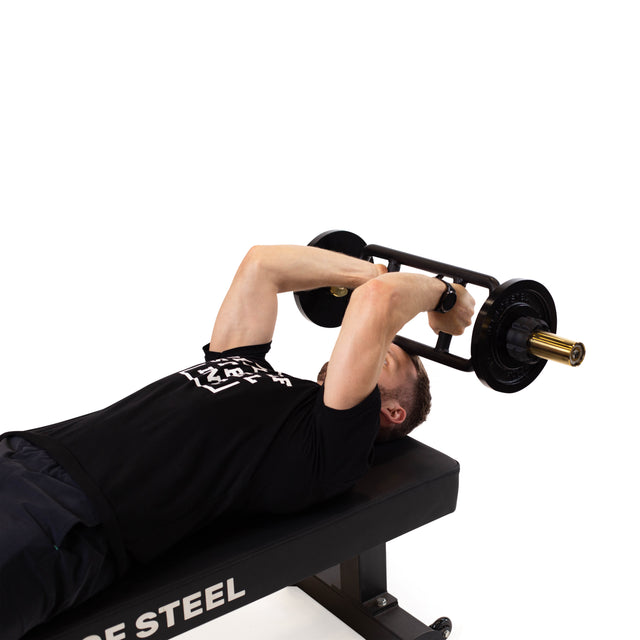 A person in a black shirt and fitness watch performs a tricep exercise, pressing the Bells of Steel Tricep Bar with ergonomic handles upwards on a bench, against a white background.