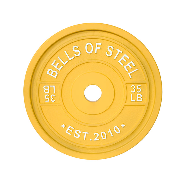 The yellow "Bells of Steel" 35 LB weight plate, featuring "EST. 2010" and a central hole for barbell loading, offers precision like the Calibrated Powerlifting Plates - LB and is ideal for organized training sessions.