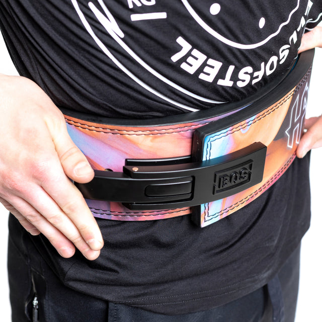 A powerlifter wears a colorful, thick Lever Belt with a large black metal buckle and "Bells of Steel" branding, secured over their waist on top of a black shirt, hands resting on their hips.