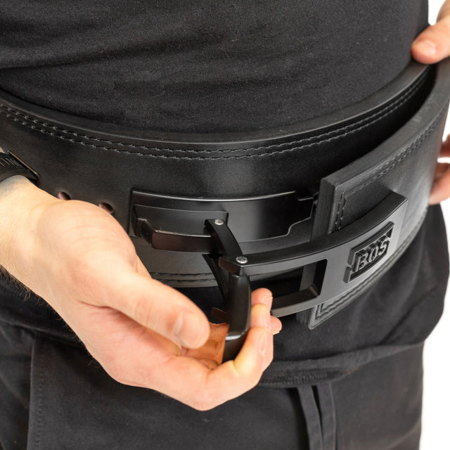 A person secures a Bells of Steel Lever Beltâa thick black lifting belt with a metal lever buckleâaround their waist, an essential step before serious powerlifting.