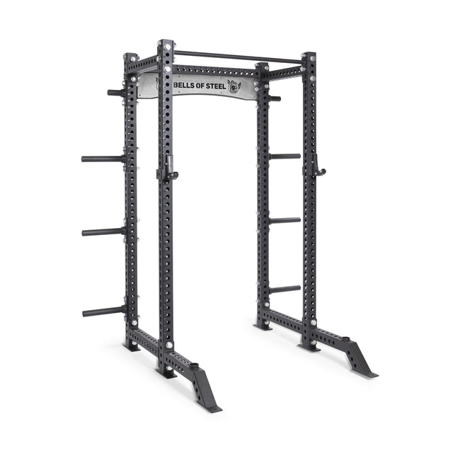 The Bells of Steel Manticore Collegiate Power Rack Builder features 3"x3" uprights, 1" holes, plate storage pegs, and a pull-up bar—ideal for any home gym setup. "BELLS OF STEEL" is labeled on the front crossbar.