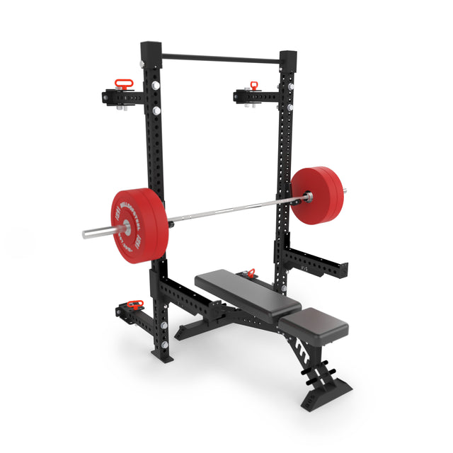 A Bells of Steel Manticore Folding Half Rack (3" x 3", 1" holes) in black is set against a white background, shown with a red barbell loaded with weight plates, an adjustable bench, and various attachments.