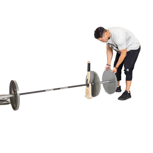 A person in athletic wear loads weight plates onto a barbell, which is propped up on the Bells of Steel Meat Hook Deadlift Jack against a white background.