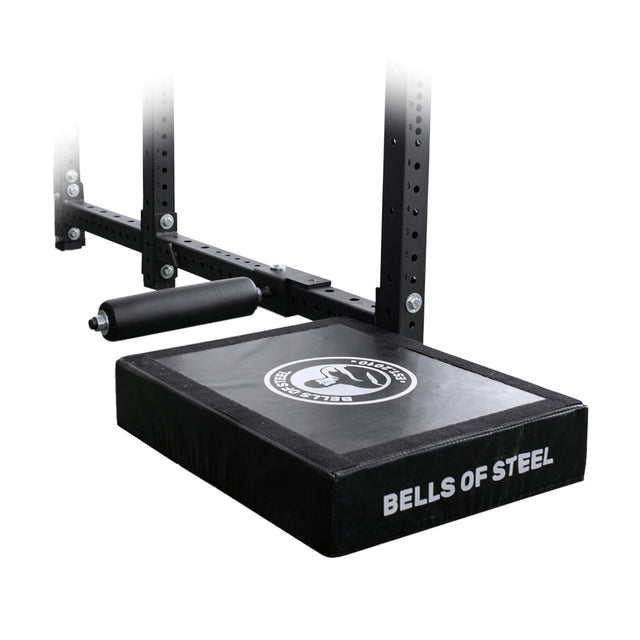 A close-up of the Bells of Steel Hydra Nordic Curl Package, a black padded attachment with "BELLS OF STEEL" on the side, mounted to a metal rack with adjustable bolts and foam roller—ideal for hamstring curls.