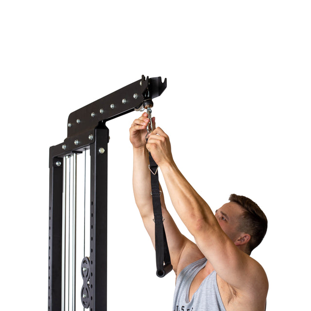 A man in a sleeveless shirt attaches a Bells of Steel Nylon Adjustable Length Single Handle Cable Attachment to a cable pulley machine against a white background.