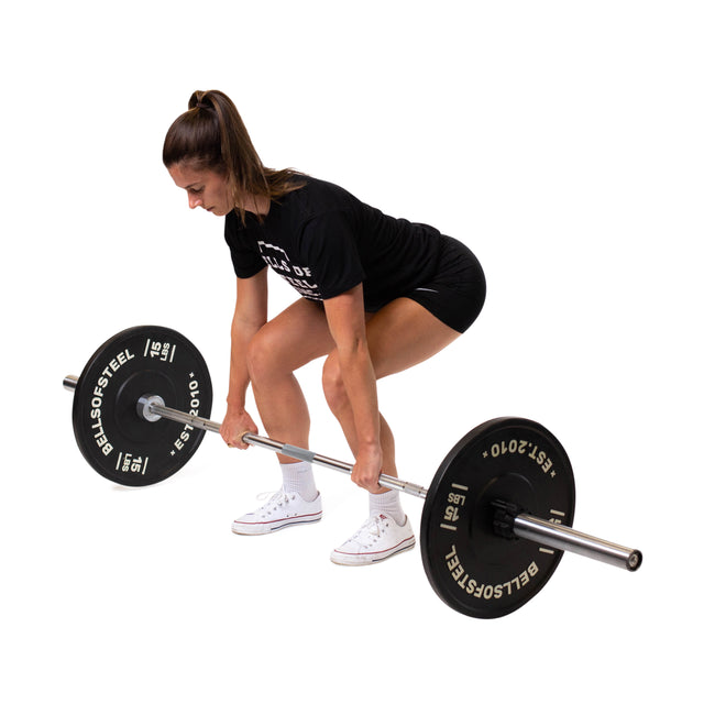 A woman in black attire and white sneakers prepares to deadlift a Bells of Steel Olympic Weightlifting Barbell with needle bearings from the floor.