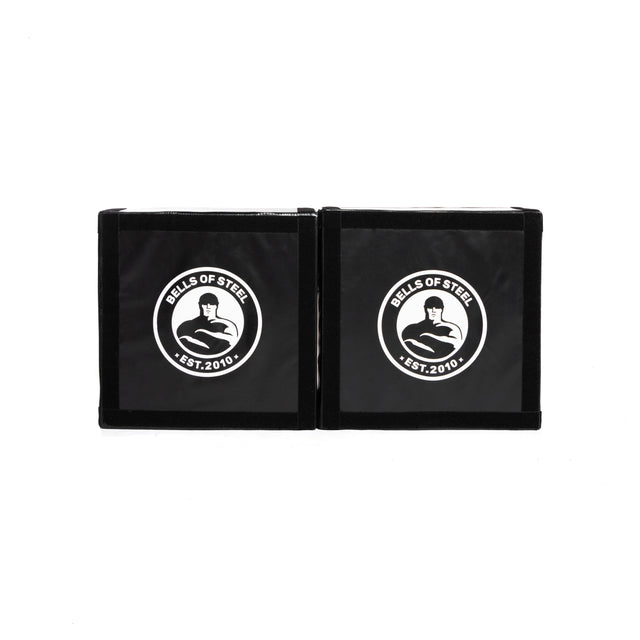 A pair of black, square Deadlift Platform Drop Pads by Bells of Steel Canada, featuring a white logo with "Bells of Steel Est. 2010" and a kettlebell design in the center, are displayed side by side on a white background. These drop pads protect floors and absorb impact, making them ideal for any intense workout session.