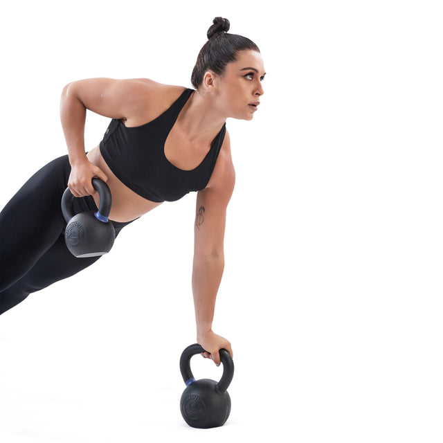 A woman in black athletic wear demonstrates strength training by performing a row with a Bells of Steel Powder Coated Kettlebell, balancing on one arm against a white background.