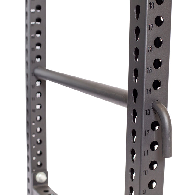 Close-up of a black metal power rack by Bells of Steel featuring Pin Pipe Safeties, numbered holes, a pull-up bar, and multiple round and keyhole openings for adjustable attachments.