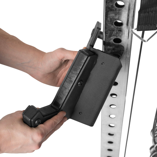 Close-up of hands adjusting a black bracket on a metallic pole with multiple holes, likely part of the Bells of Steel Functional Trainer Cable Tower, highlighting gym equipment versatility and potential for conversion kit enhancements.