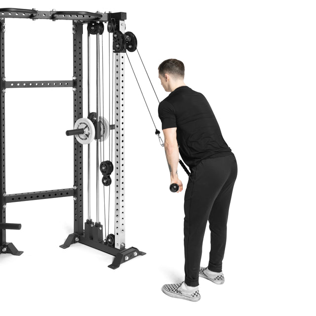 A person dressed in black uses the Bells of Steel Functional Trainer Cable Tower for tricep pushdowns, standing while holding the bar with both hands to pull it down. The plain white background accentuates the sleek modern design of this cable tower.