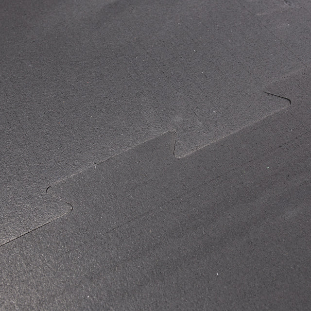 Close-up of the textured surface and zigzag interlocking edge of a Bells of Steel Black Puzzle Mat, highlighting how two pieces connect securely.