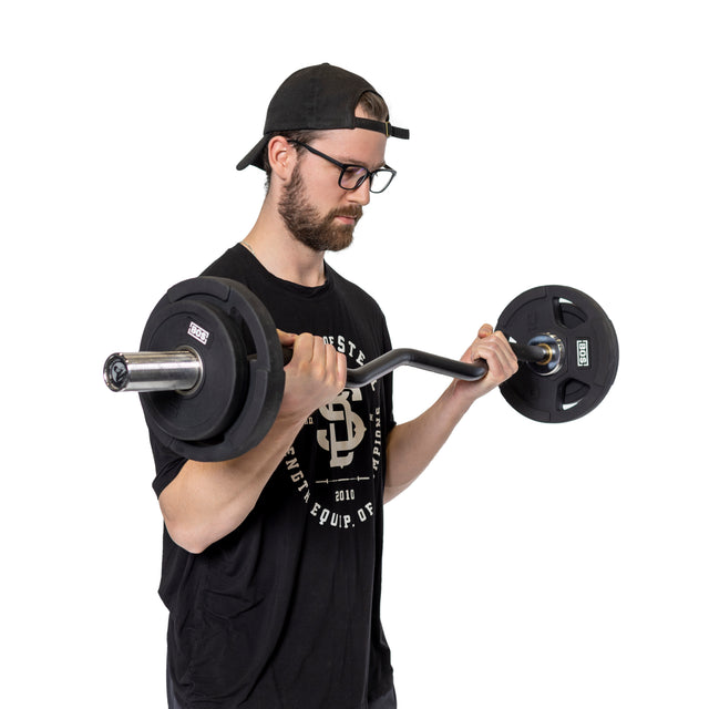 A person in a black t-shirt, cap, and glasses performs a bicep curl with Bells of Steel's Rubber Coated Iron Weight Plate Sets on a barbell. They are against a plain white background, focused on the exercise.