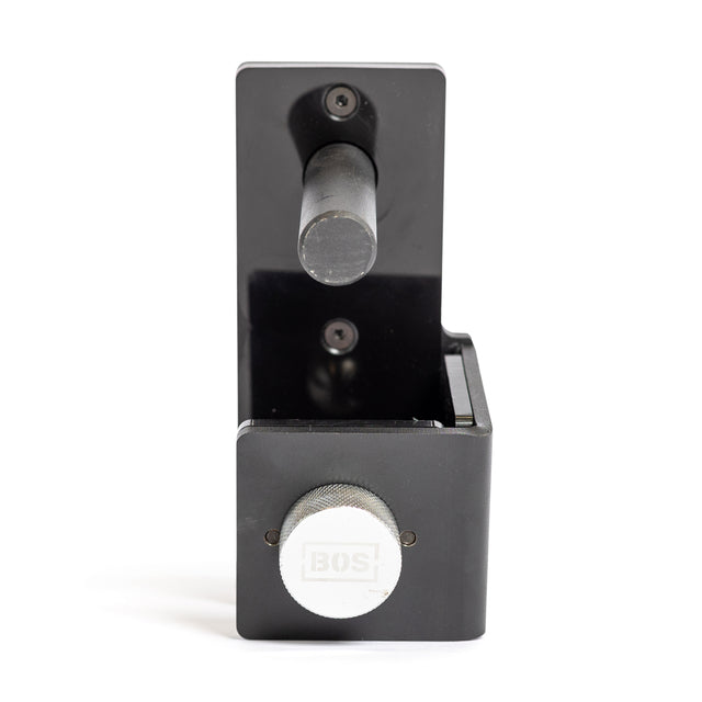 A black metal Roller J-Cup by Bells of Steel, featuring a cylindrical handle, rectangular body, and large silver adjustment knob labeled "BOS!”, designed to protect barbells during bench press, is shown against a white background.