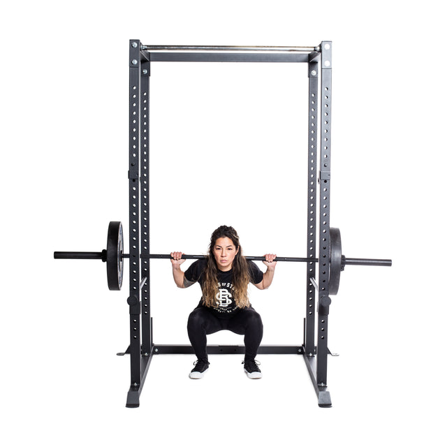 A woman with long hair squats with a weighted barbell on her shoulders inside the Bells of Steel Residential Power Rack (2.3" x 2.3", ⅝" holes), using j-cups for support, wearing black workout attire against a plain white background—ideal for home gyms.