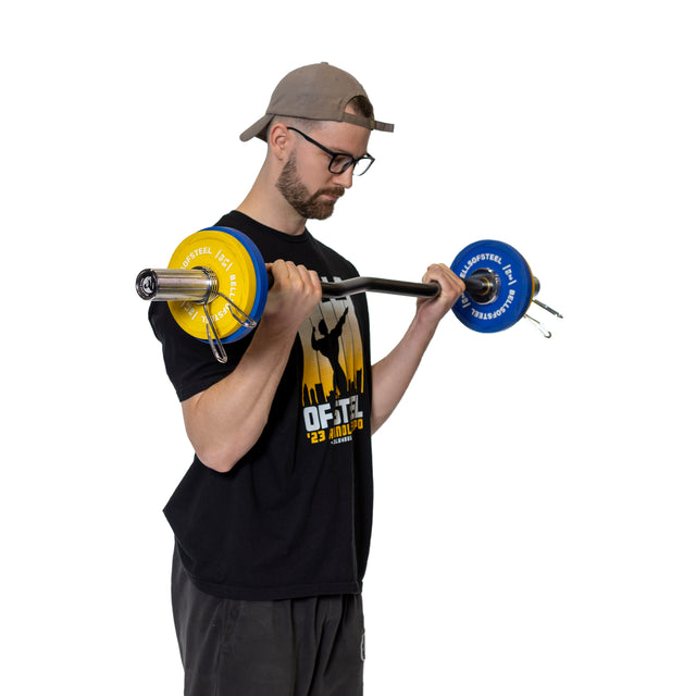 Wearing a cap and glasses, a person in a black T-shirt is performing bicep curls with a barbell. Bells of Steel Spring Collars secure the yellow and blue weight plates on the polished chrome Olympic barbell sleeves against a plain white background.