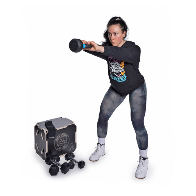 A woman in athletic wear swings a steel mace with both hands. Next to her are dumbbells, a cube-shaped device, and other Bells of Steel Strength Circuit Starter Kits—ideal for effective home workouts on a white background.