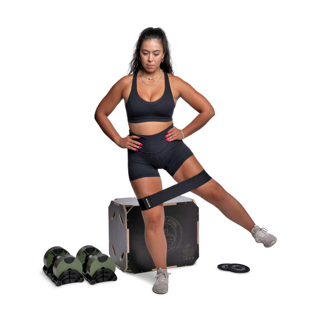 A woman in black athletic wear demonstrates a lateral leg raise with a resistance band and Bells of Steel Strength Circuit Starter Kits, which include dumbbells, a plyo box, weights, and a gliding disc, all on a white background.