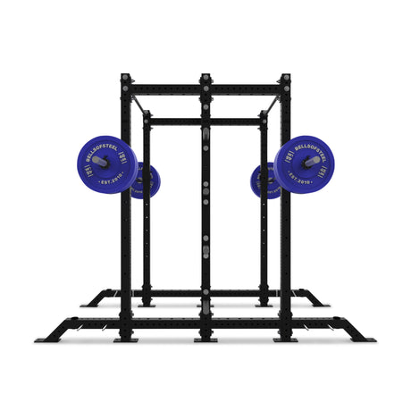 The Bells of Steel Hydra 2-Sided Rack is a black metal modular power rack with four vertical posts and two blue barbells on each side, ideal for weightlifting, strength training, or team workouts.