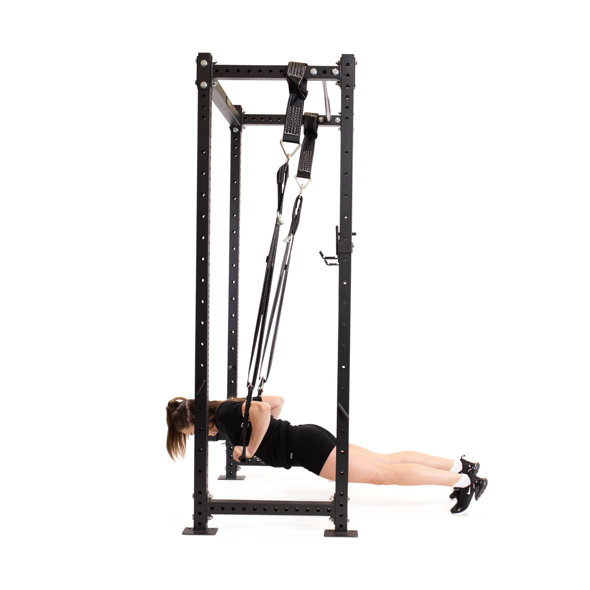 Using the Bells of Steel Suspension Spotter Straps and Bodyweight System, a person executes a standing cable press within the black metal frame. The safety spotter straps ensure secure arm movements as resistance bands are held and extended forward.