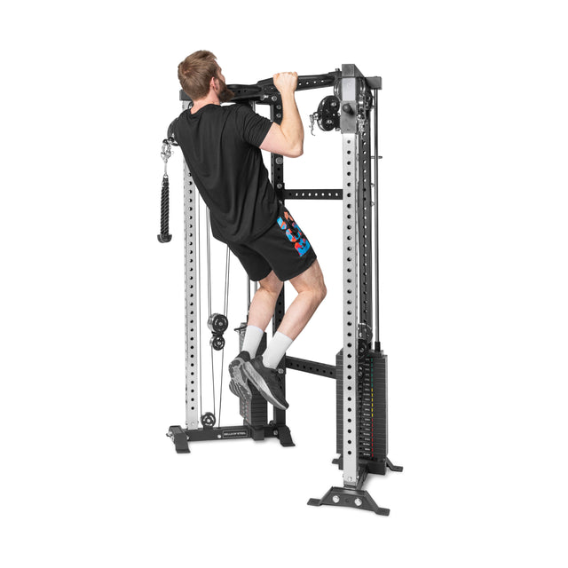 Someone in athletic wear is doing pull-ups on the Bells of Steel Functional Trainer Cable Tower, which features multiple weight settings and various pulleys and handles.