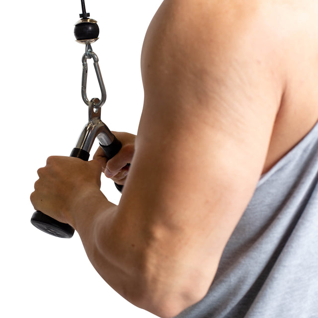 A person in a sleeveless shirt, seen from the back, prepares to use the Bells of Steel Tricep Pressdown With Ergo Handgrips on a cable machine against a white background.