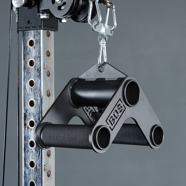 A close-up of the Bells of Steel Fat Bar - T-Bar Row Cable Attachment, a black metal grip strength tool, hangs from a carabiner with its engraved branding visible against a gray background.