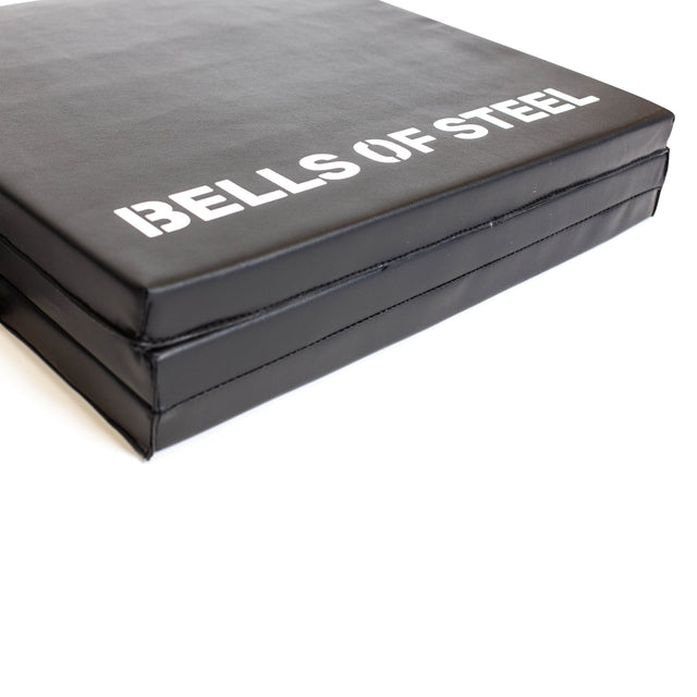 A close-up of the Bells of Steel Trifold Mat, a black non-slip exercise mat with "BELLS OF STEEL" printed in white on the surface.