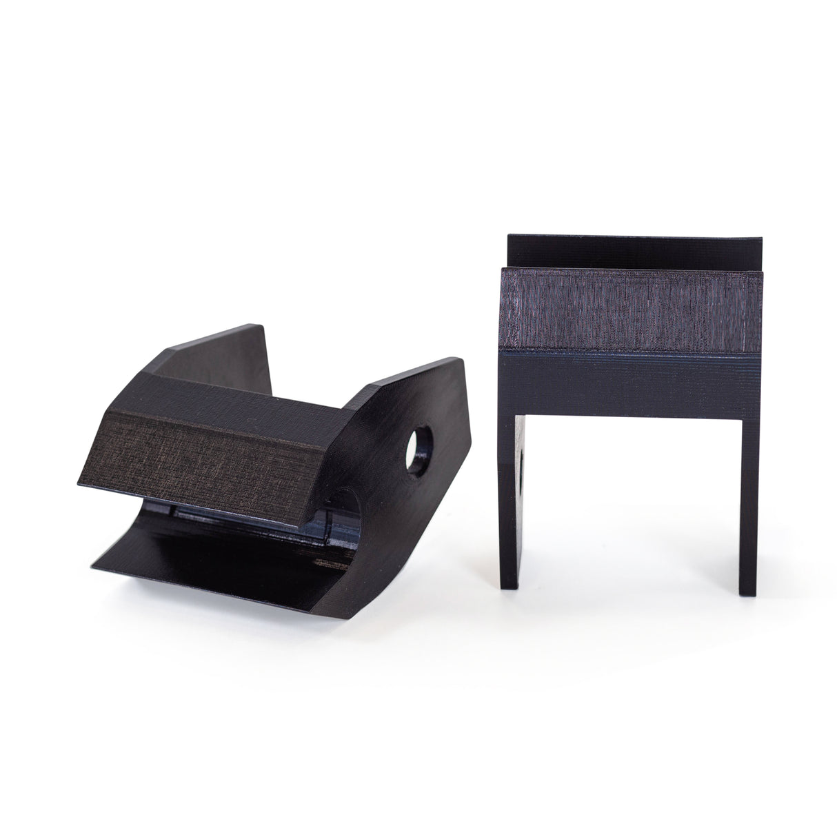 Two black, geometric Above Rack Barbell Holder parts by Bells of Steel stand upright on a white background—one is angled with a hole like a barbell holder, the other stands vertically with two legs.
