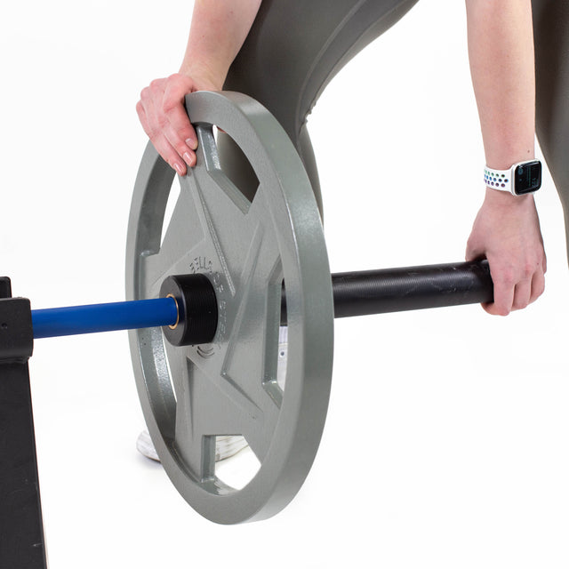 Wearing an Apple Watch, a person adjusts a Bells of Steel Mighty Grip Olympic weight plate on an ergonomically designed barbell, partially resting on a stand against a white background.