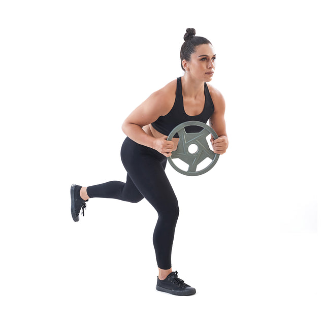 A woman in black athletic wear uses a Gray Mighty Grip Olympic Weight Plate from Bells of Steel for her exercise. Balancing on one leg with precision grip handles for enhanced control, she stands focused and isolated against a white background.