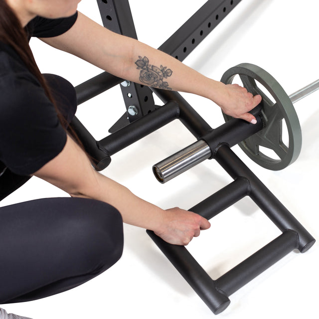 A person with a floral forearm tattoo loads a weight plate onto a 2" Olympic bar attached to the Bells of Steel Viking Press Attachment, getting ready for an intense landmine workout.