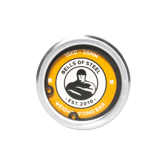 A close-up of the end cap on the Bells of Steel Oly Lifting Needle Bearing Bar - Women's, showing the logo with a muscular figure, "15KG - 25MM," and "Weightlifting Bar Est. 2010" on a yellow background and 25mm shaft.