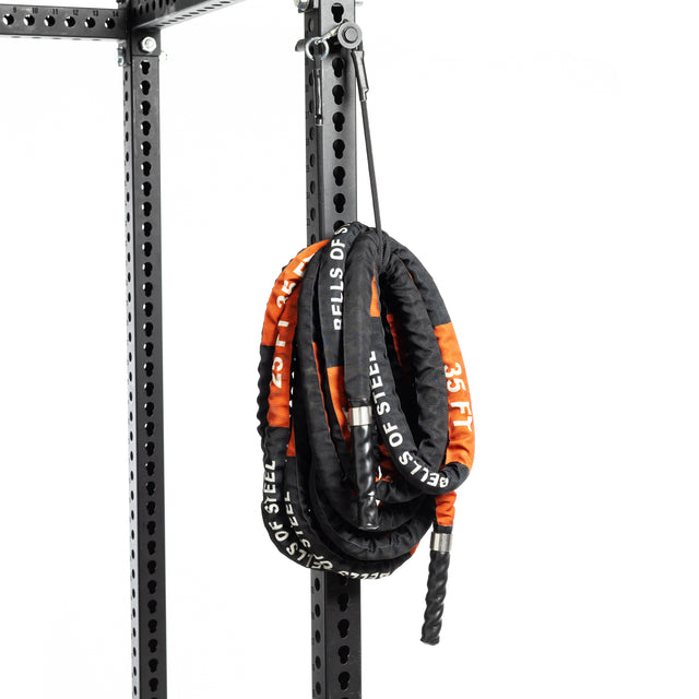 A Bells of Steel Battle Rope, coiled with a protective cover, hangs from a black metal gym rack against a white backdrop. The rope is perfect for conditioning workouts and features the text "BELLS OF STEEL 25 FT.