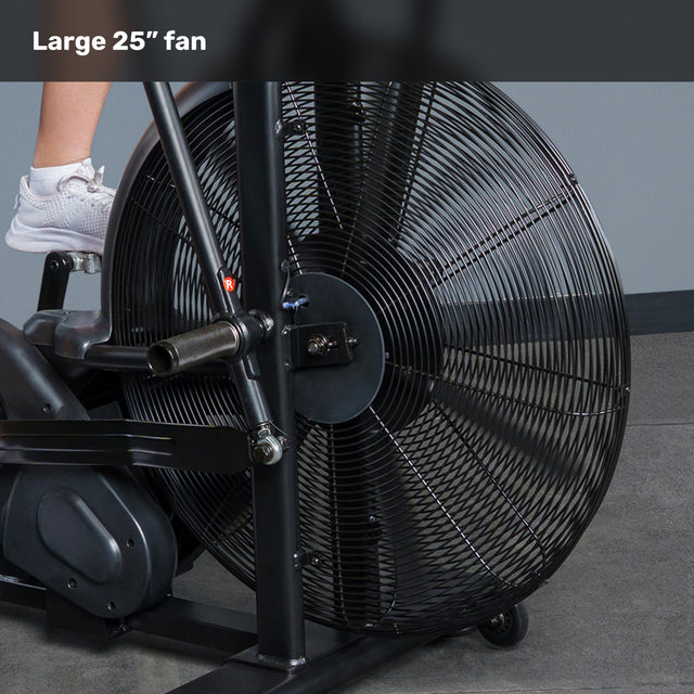 A close-up of the Bells of Steel Blitz Air Bike’s large 25-inch fan, partly showing a person’s leg and white shoe on the pedal. The commercial-grade fan blades are safely enclosed in a sturdy black metal grill.