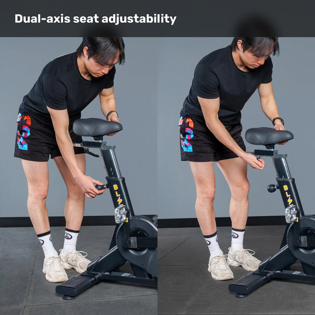 A person demonstrates the dual-axis seat adjustability of the Bells of Steel Blitz Air Bike, wearing a black shirt, patterned shorts, white socks, and sneakers.