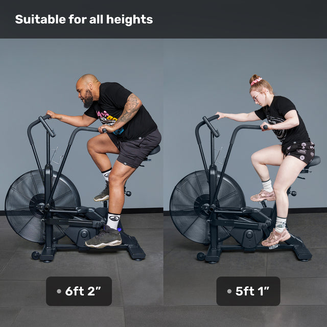Two riders, one 6'2" and the other 5'1", pedal together on the Bells of Steel Blitz Air Bike in a gym. Above them, text reads "Suitable for all heights." This commercial-grade air bike easily fits users of varying sizes.