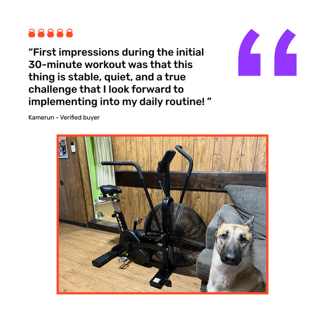 A Bells of Steel Blitz Air Bike stands in a wood-paneled room beside a brown couch where a dog sits. Above the commercial-grade bike, a customer review appears in bold text.
