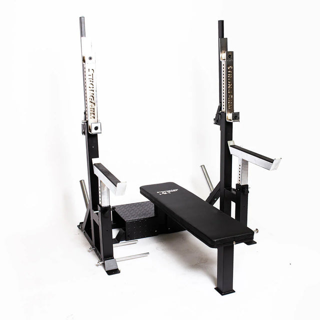 The Bells of Steel StrongArm Combo Rack - Squat Stand & Bench Press features a black and silver adjustable frame with padded bench, metal bar holders, and safety arms, ideal for strength training. Shown against a plain white background.