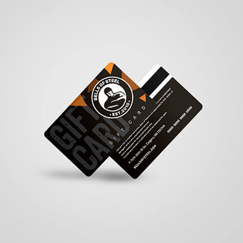 The Bells of Steel Canada Gift Card, established in 2010, showcases overlapping cards with black and orange design elements featuring the "Bells of Steel" brand on one side and card information with a magnetic stripe on the other, ideal for anyone ready to make gainz.