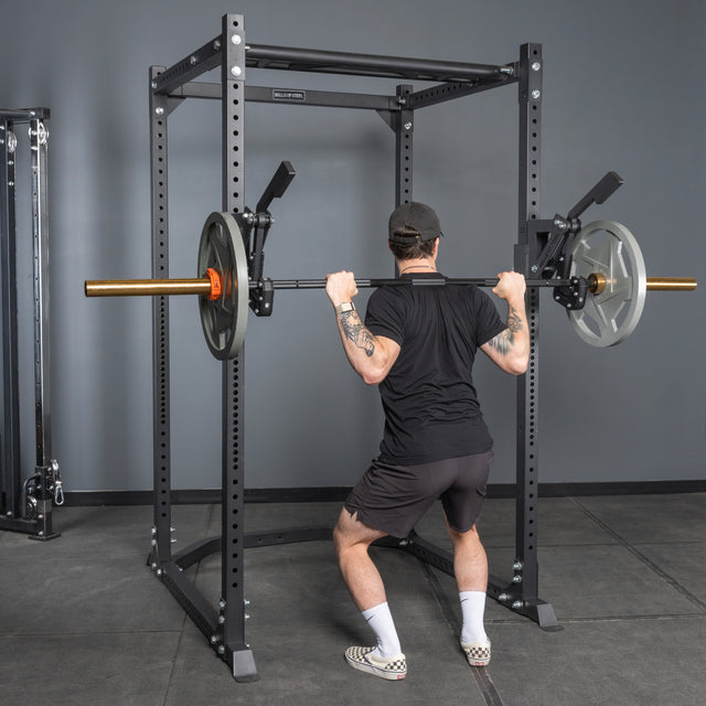 A person performs a squat with a barbell inside a power rack equipped with the Bells of Steel Monolift Rack Attachment, highlighting this practical gym accessory in action.